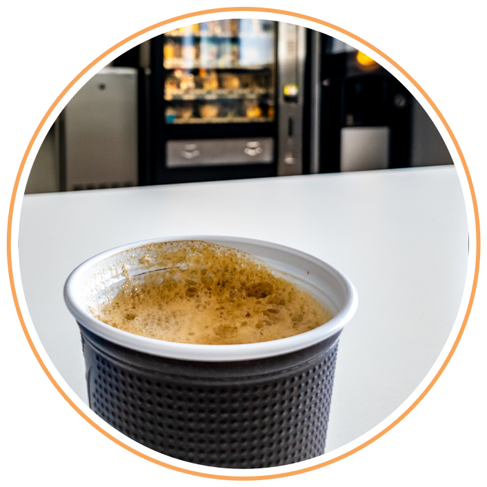 Cup of coffee resting on a white table with a vending machine in the background.