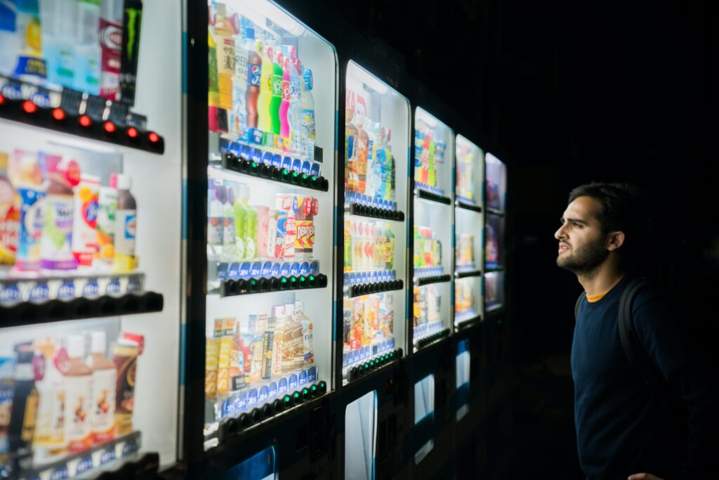 A man looks at a row of vending machines full of food and beverages. Photo by Victoriano Izquierdo on Unsplash.